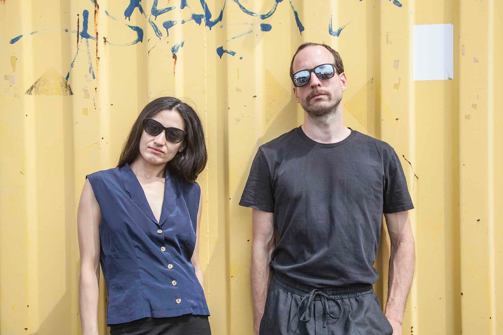 should-I-know pose with sunglasses in front of a yellow container wall.