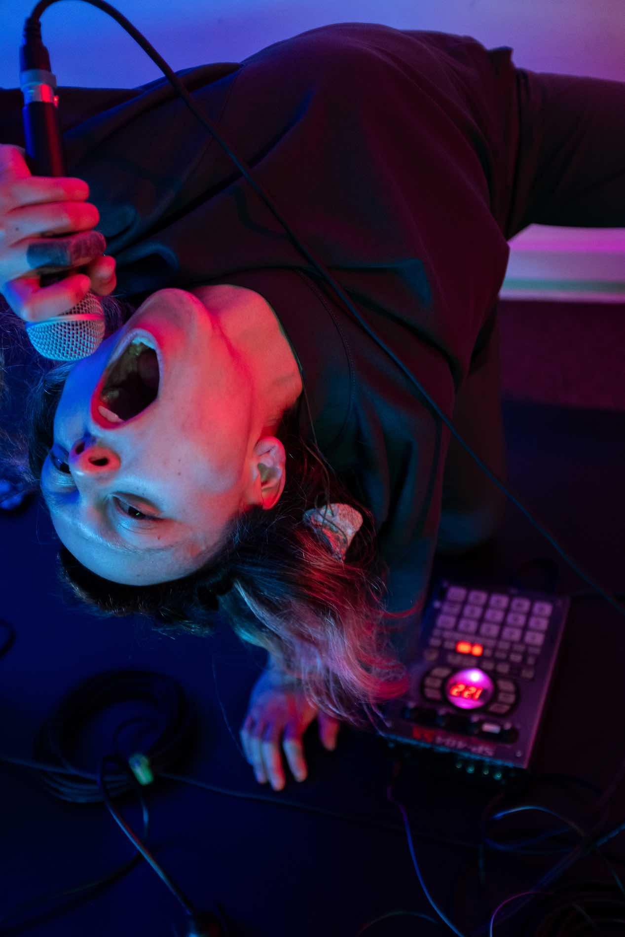 Standing over a mixing desk with his back bent backwards, a person shouts into a microphone.