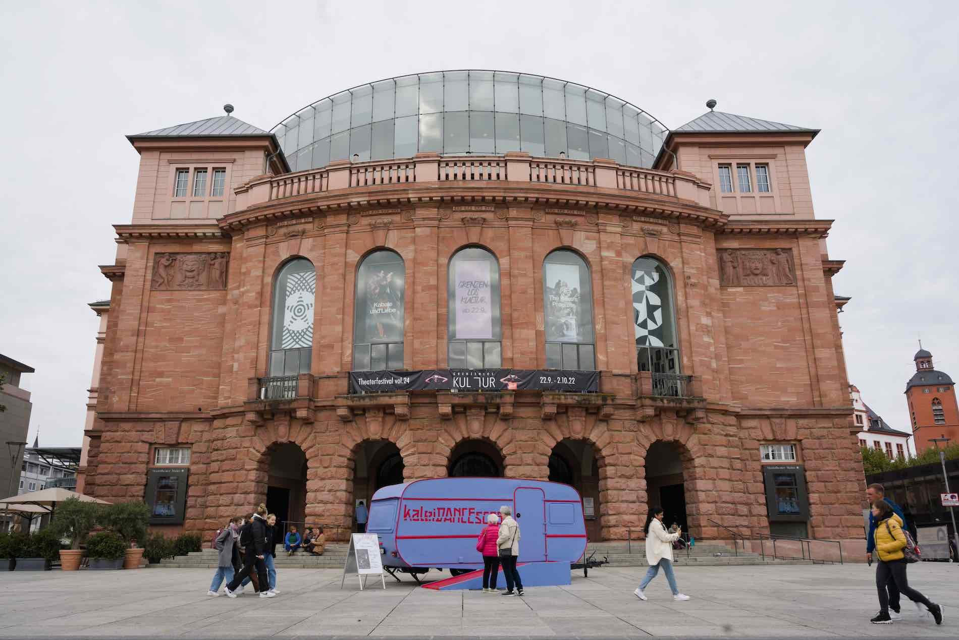 The kaleiDANCEScope caravan stands in front of the imposing Staatstheater in Mainz. The building is made of reddish stone and has a round front inspired by the Colosseum in Rome.
photo: Cornelius Schaper
