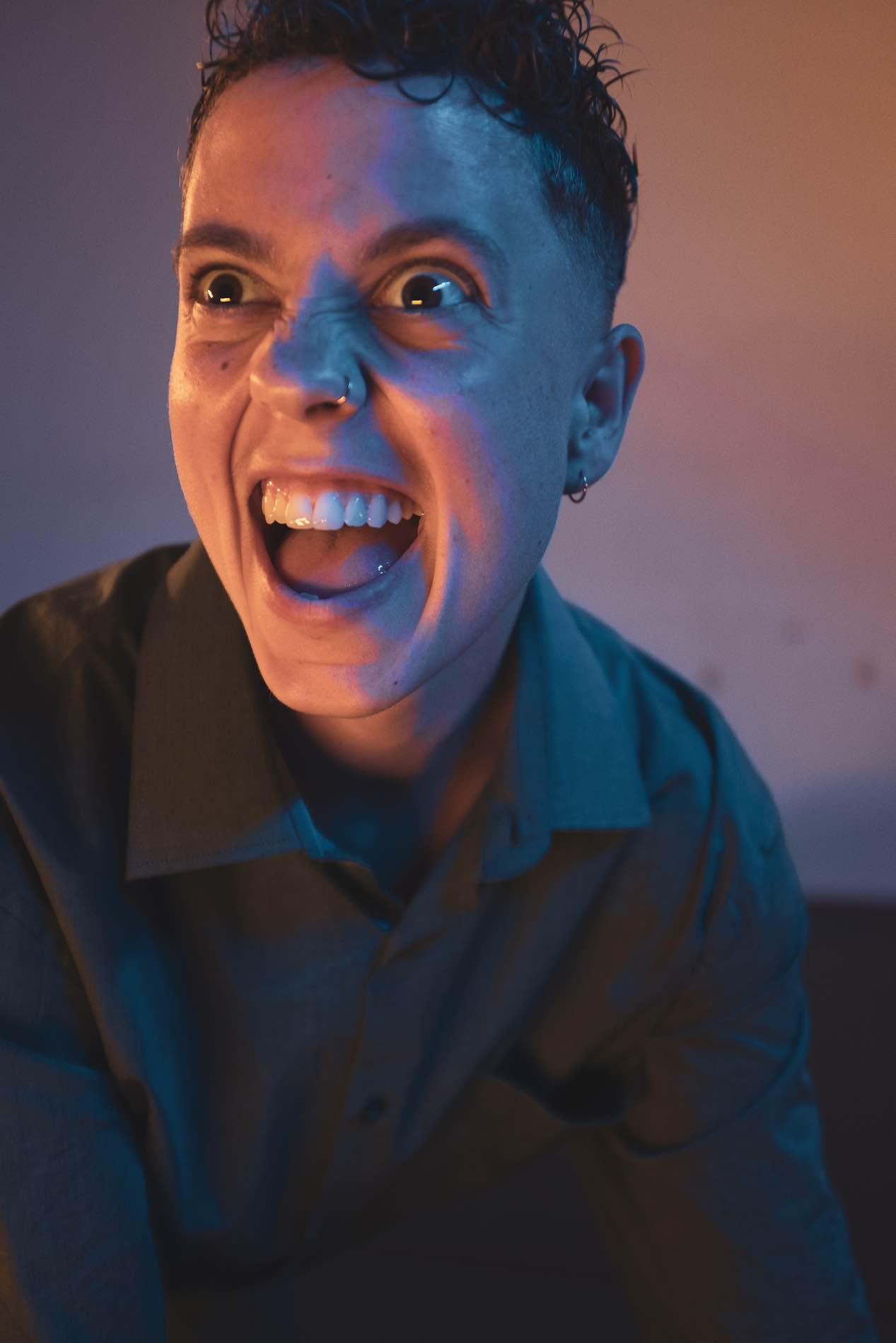 A face in blue-orange light grimaces and looks menacingly towards the audience.