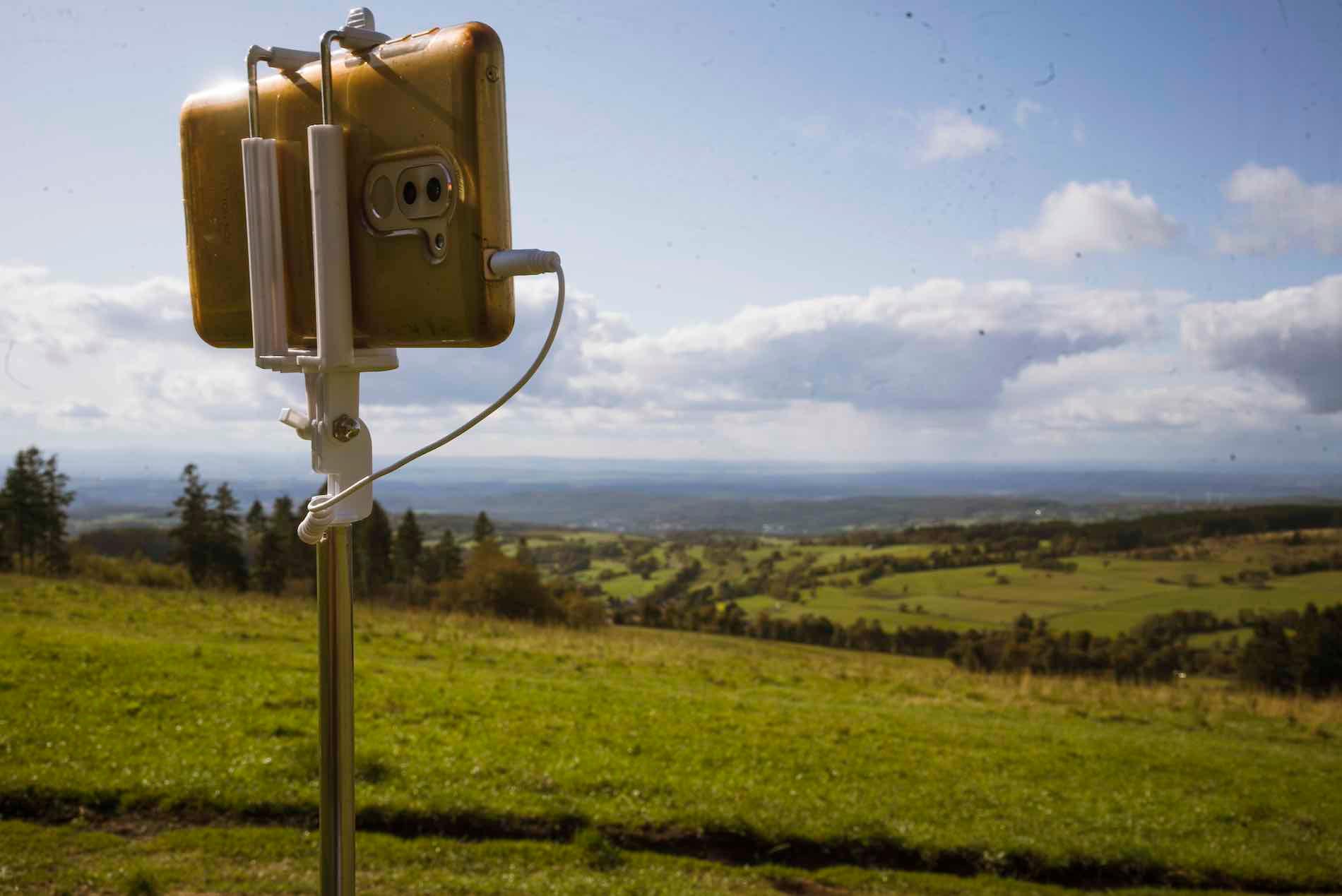 Ein Smartphone auf einem Selfie-Stick blickt auf ein hügeliges Panorama.
Foto: should-I-know